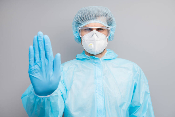 Photo of guy expert doc virologist hold palm stop patients stepping into danger infected zone wear gloves mask hazmat blue uniform surgical cap goggles isolated grey color background - Fotografie, Obrázek