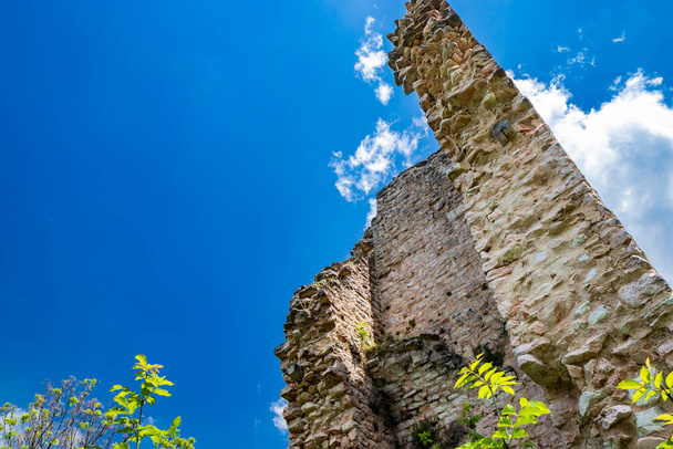 A ruína da torre de menagem do castelo de Trinci em Rasiglia. Os restos da torre, cobertos por vegetação, agora desabaram e quase completamente destruídos. O céu azul com nuvens. Foligno, Umbria, Itália
 - Foto, Imagem