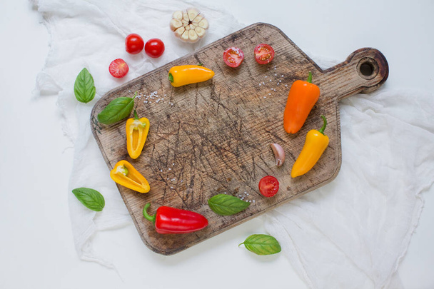Овощная рама, деревянная разделочная доска с перцем, помидоры, чеснок, базиликовые листья и морская соль
 - Фото, изображение