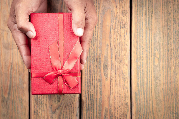 Top kilátás a kezek kezében piros ajándék doboz fa asztalon. Karácsony, Szilveszter, Valentin-nap, Születésnap és különleges alkalmak koncepció. - Fotó, kép
