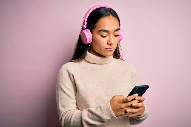 Giovane bella donna asiatica che ascolta musica utilizzando smartphone e cuffie con un'espressione sicura sul viso intelligente pensando seriamente
 - Foto, immagini