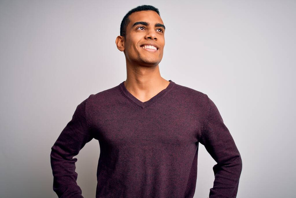 Young handsome african american man wearing casual sweater over white background looking away to side with smile on face, natural expression. Laughing confident. - Zdjęcie, obraz