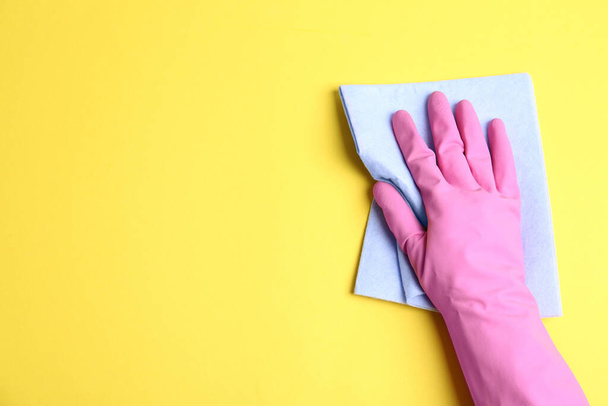 Person in rubber glove with rag on yellow background, closeup of hand. Space for text - Fotó, kép