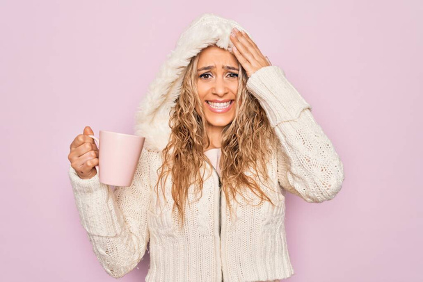 Young beautiful blonde woman wearing casual sweater with hood drinking cup of coffee stressed and frustrated with hand on head, surprised and angry face - Photo, Image