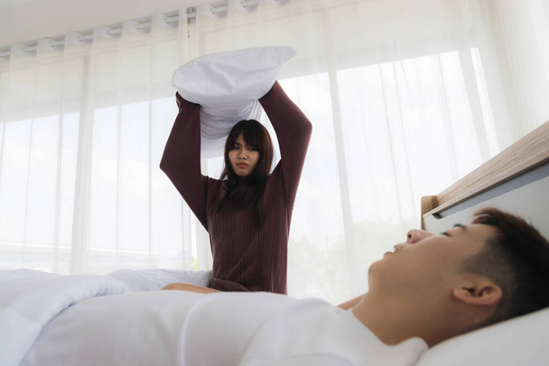Aasialainen vaimo käyttää tyyny lyödä miehensä, koska hän on ärtynyt hänen kuorsaus. Avioelämän ongelmien käsite avioliiton jälkeen - Valokuva, kuva