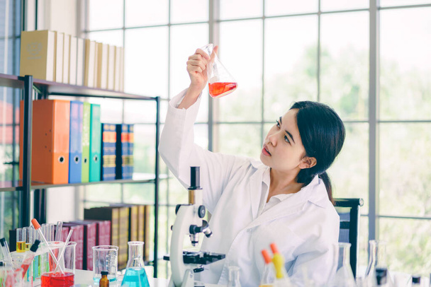Nuoret tutkijat tutkivat punaisia kemikaaleja dekantterilasissa.. - Valokuva, kuva