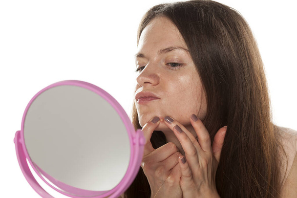 mladá žena bez make-upu se dívá do zrcadla a mačkání její pupínky - Fotografie, Obrázek