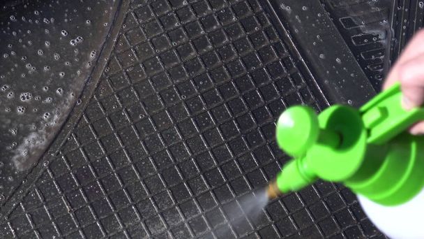 Un hombre pone espuma en una alfombra de coche para eliminar la suciedad. Detergente especial para lavado de autos
. - Foto, imagen