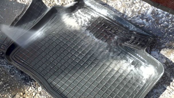 Nettoie la saleté d'un tapis de voiture avec un jet d'eau haute pression. Détergent spécial pour lavage de voiture
. - Photo, image