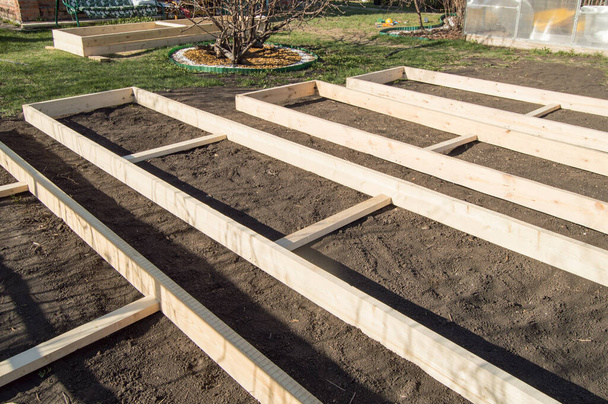 Ξύλινη μορφοποίηση από νέες σανίδες για φυτικές παρτέρια στον κήπο, προετοιμασία και κατασκευή, ξυλουργική. - Φωτογραφία, εικόνα