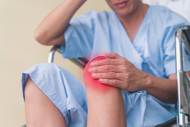 Zbliżenie męskich pacjentów na wózkach inwalidzkich używa dłoni do przytrzymania bólu kolana. - Zdjęcie, obraz