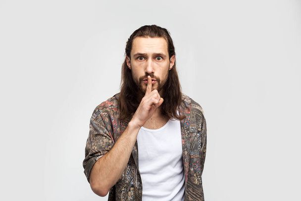 Request for silence. Dumb man, demands silence gesture and be quieter. Hipster traveler stylish carefree man on a white studio background, people lifestyle - Zdjęcie, obraz