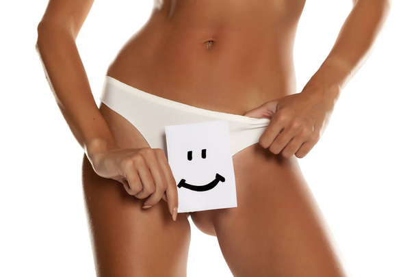 Woman with panties cowers her vagina with smile drawn on sheet of paper on white background - Fotó, kép