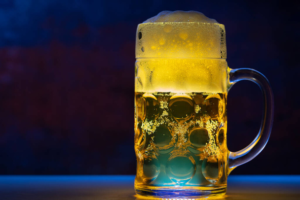 Glass tankard of golden ale on a counter top in blue toned light with copy space conceptual of nightlife or a club - Foto, Imagem