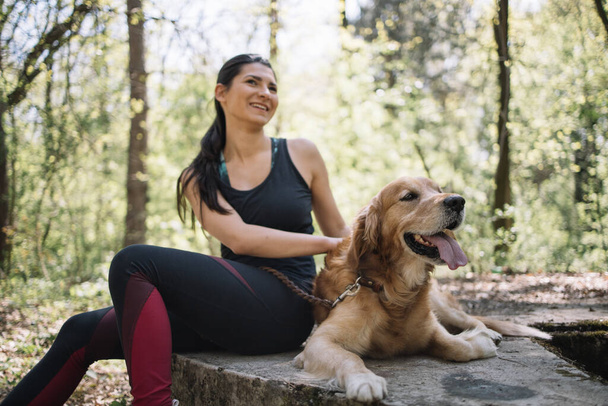 Out of focus girl in sportswear sitting in park with dog - 写真・画像