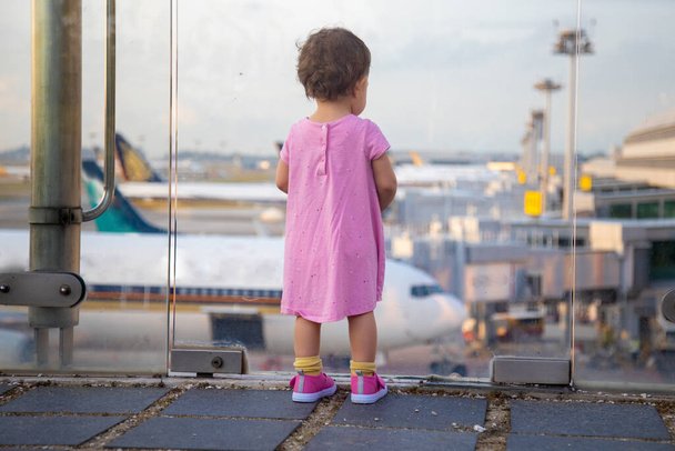 bebé pequeño pasajero infantil mira los aviones en el aeropuerto. vista posterior
 - Foto, imagen