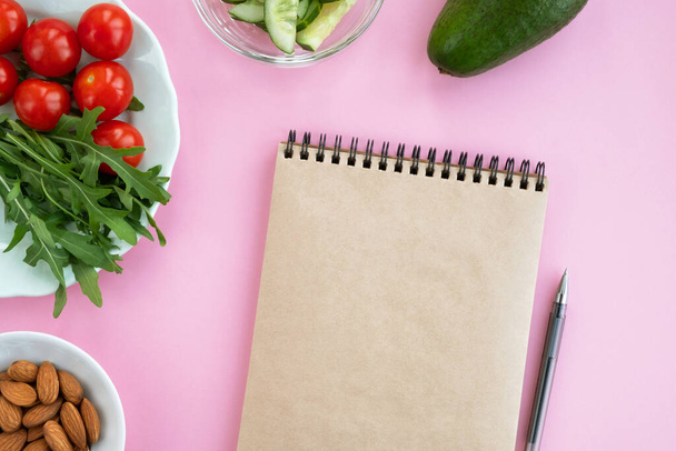 Concepto de dieta. Cuaderno, verduras frescas y frutos secos sobre fondo rosa. Vista superior, plano, espacio para copiar
 - Foto, imagen