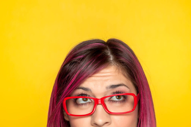 Mezzo ritratto di una giovane donna preoccupata con capelli rosa e occhiali su sfondo giallo
 - Foto, immagini