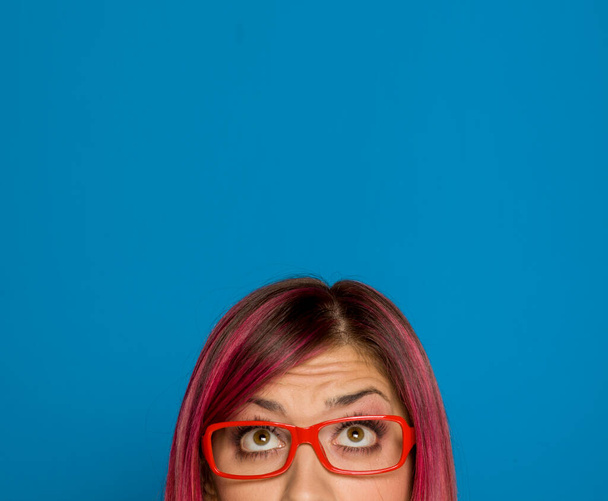 Half portrait of a young worried woman with pink hair and glasses on blue background - Photo, Image