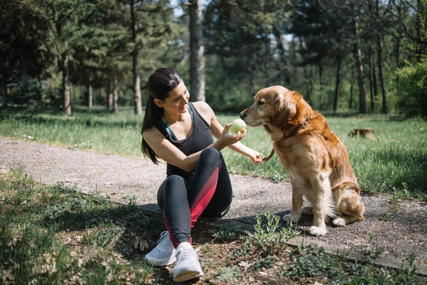 Pretty woman sitting on ground with dog and holding ball - Fotografie, Obrázek