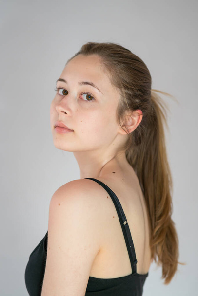 Portrait of a pretty teenage girl with long natural blonde hair and smooth skin looking at the camera. Studio shot - Photo, Image