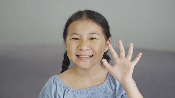 Cute asian little girl smiling and waving hand looking at camera at home - Photo, Image