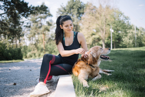 Beautiful woman sitting on ground in park with dog - 写真・画像