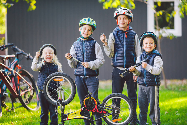 Mechanika dziecięca, naprawa rowerów. Szczęśliwe dzieci naprawiają rower razem na świeżym powietrzu w słoneczny dzień. Koncepcja naprawy rowerów. Rodzina pracy zespołowej pozowanie z narzędziami do naprawy roweru w rękach na zewnątrz. - Zdjęcie, obraz