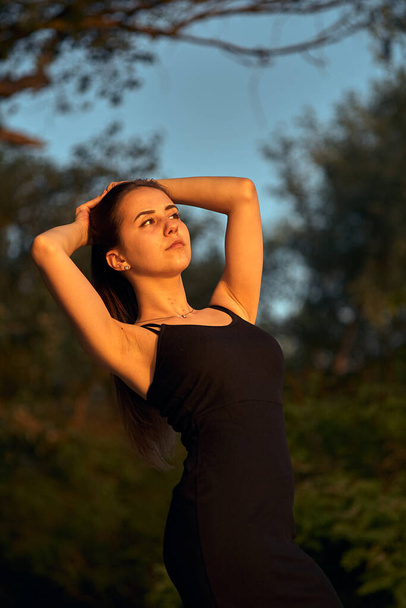 Beautiful girl on the nature near the green shore. Enjoys the setting sun. The concept of outdoor recreation, a walk in the park. Relaxation from the bustle of the city. - Фото, зображення