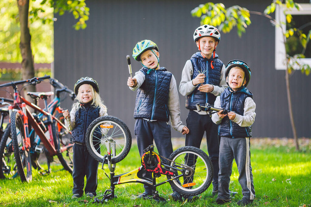 Children mechanics, bicycle repair. Happy kids fixing bike together outdoors in sunny day. Bicycle repair concept. Teamwork family posing with tools for repairing a bicycle in hands outside. - Photo, Image
