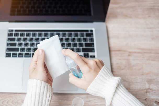 Γυναίκα καθαρισμού laptop με υγρά μαντηλάκια ιστού και απολυμαντικό αλκοόλ στο χώρο εργασίας κατά τη διάρκεια της εργασίας και online μάθησης στο γραφείο στο σπίτι, προστασία coronavirus (Covid-19) λοίμωξη. Νέα κανονική έννοια - Φωτογραφία, εικόνα