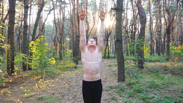 Jongeman aan het trainen in een prachtig zonnig bos. Flexibele gymnastiektraining in een schilderachtige omgeving. Atleet het verhogen van handen tonen yoga oefeningen buiten. Concept van een gezonde en actieve levensstijl. - Foto, afbeelding