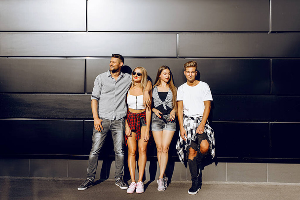 A group of young friends, girls and boys pose together against a black wall in the city - Fotoğraf, Görsel