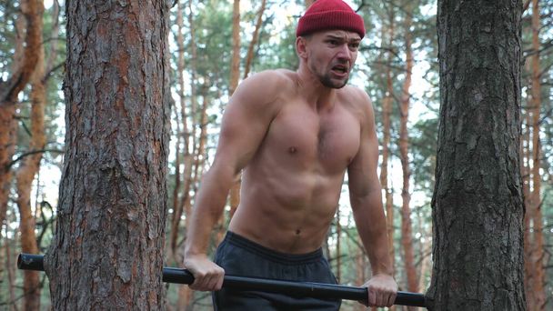 Strong and muscular man doing push ups on horizontal bar in forest. Hardy sportsman working out at nature. Athletic guy training outdoor. Concept of sport and active lifestyle. Close up Slow motion. - Photo, Image