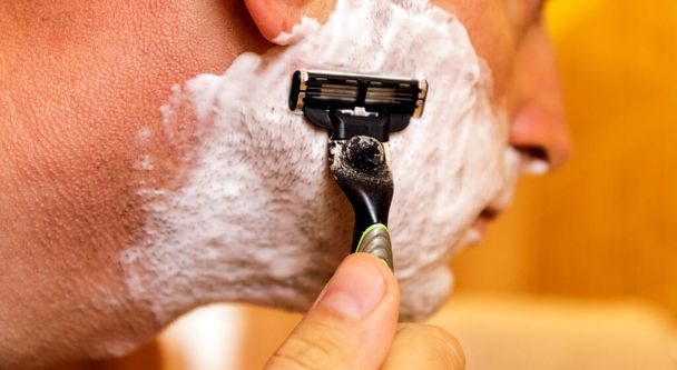 Homem rapando o rosto com a lâmina de barbear através de espuma de barbear. Homens cuidados com a pele conceito
. - Foto, Imagem