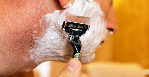 Muž si holí obličej břitvou přes pěnu na holení. Mužská péče o pleť koncept. - Fotografie, Obrázek