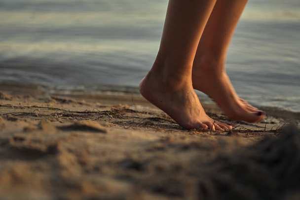 Female feet barefoot on a sandy beach in the water. Close-up of beautiful female legs. Wet foot. - Фото, изображение