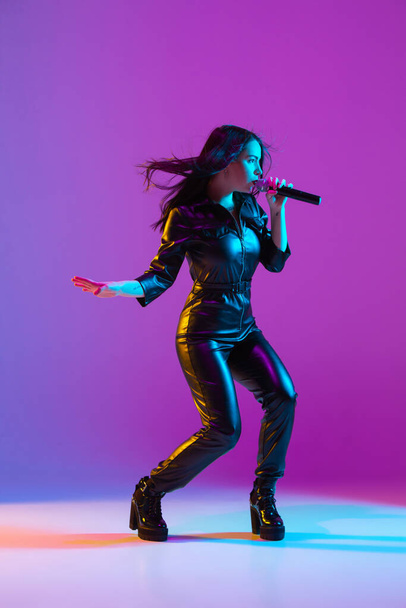 Caucasian female singer portrait isolated on purple studio background in neon light - Foto, Bild