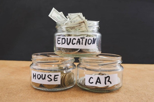 Glass cans with dollars and text: home, cars, education. Concept of saving money. - Fotoğraf, Görsel