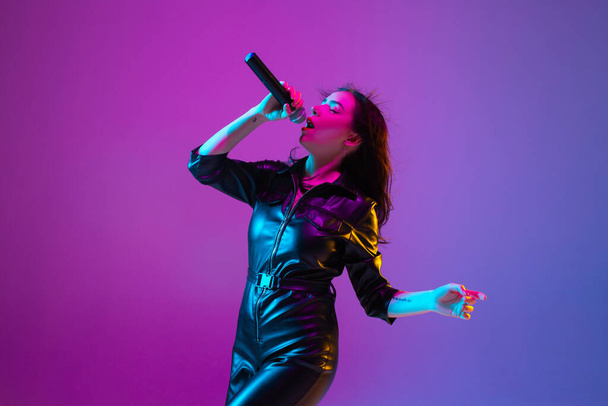 Caucasian female singer portrait isolated on purple studio background in neon light - Fotografie, Obrázek