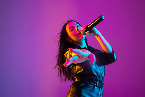 Caucasian female singer portrait isolated on purple studio background in neon light - 写真・画像
