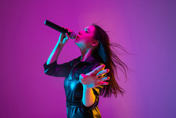 Caucasian female singer portrait isolated on purple studio background in neon light - Foto, Bild
