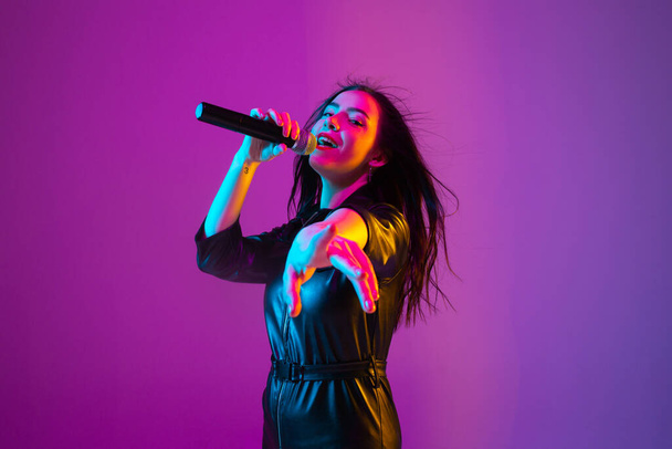 Caucasian female singer portrait isolated on purple studio background in neon light - Fotó, kép