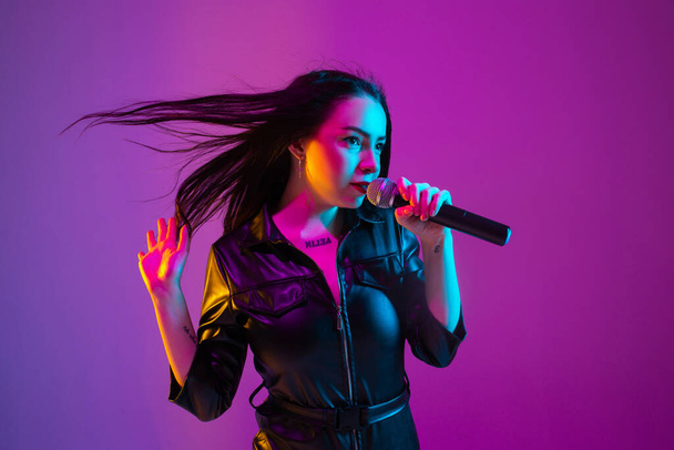 Caucasian female singer portrait isolated on purple studio background in neon light - Foto, immagini