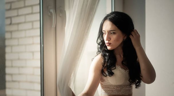 Uzun siyah saçlı, dantel elbiseli güzel kız pencereye yaslanmış. - Fotoğraf, Görsel
