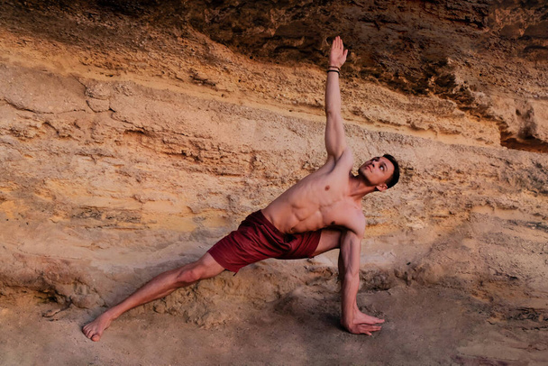 Fit gespierde man doet yoga in de buurt van de berg. Pilates krijger poseren gezonde wervelkolom workout. monochroom beige. Een man die zijn hand uitstrekt naar de hemel en omhoog kijkt. concentratie balans pilates kunst  - Foto, afbeelding