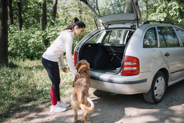 Young woman standing with her dog near car with opened trunk - Foto, immagini
