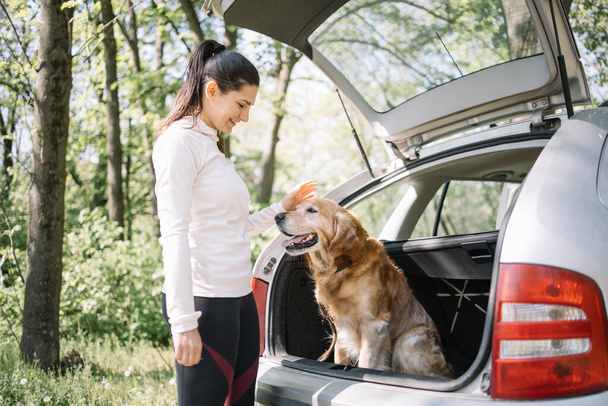 Smiling woman petting dog in opened trunk - Фото, изображение