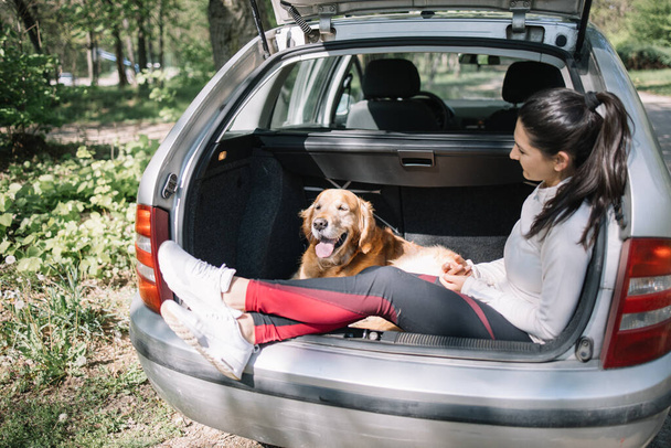 Woman and dog sitting in opened car trunk - Φωτογραφία, εικόνα