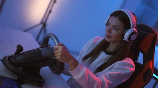 A menina gamer joga jogos de vídeo com volante na sala de luz azul
 - Filmagem, Vídeo